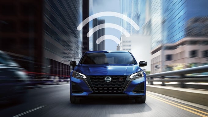 Vue de face d’une Nissan Altima 2024 bleue roulant sur fond flou et d’un logo de Wi-Fi surmonté de trois lignes courbes.