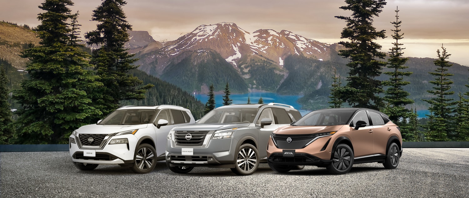 Nissan Rogue et Nissan Pathfinder garés côte à côte en face d’arbres et de montagnes rocheuses.