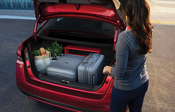 Illustration de la Nissan Versa 2023 montrant une personne qui referme le coffre contenant des bagages et des sacs d’épicerie.